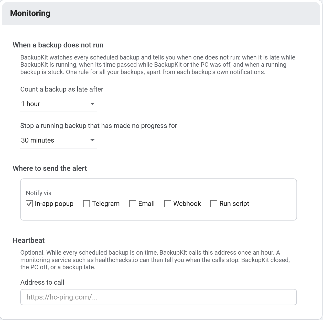 BackupKit's Monitoring settings: count a backup as late after 1 hour, stop a running backup that has made no progress for 30 minutes, where to send the alert (in-app popup, Telegram, email, webhook or a script), and an optional heartbeat address such as healthchecks.io